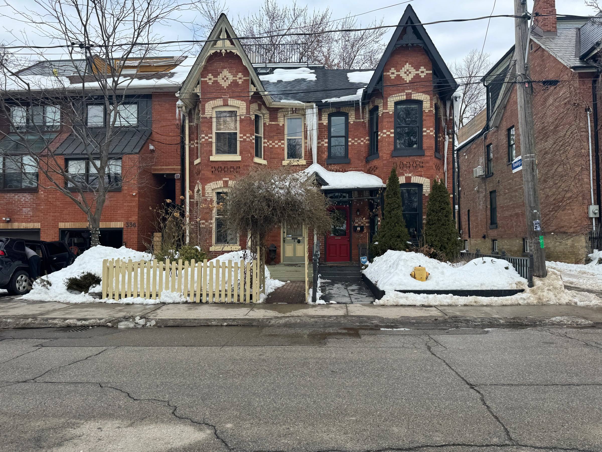 Victorian red-brick row houses with decorative gables and a picket fence in Cabbagetown, after a snowfall.