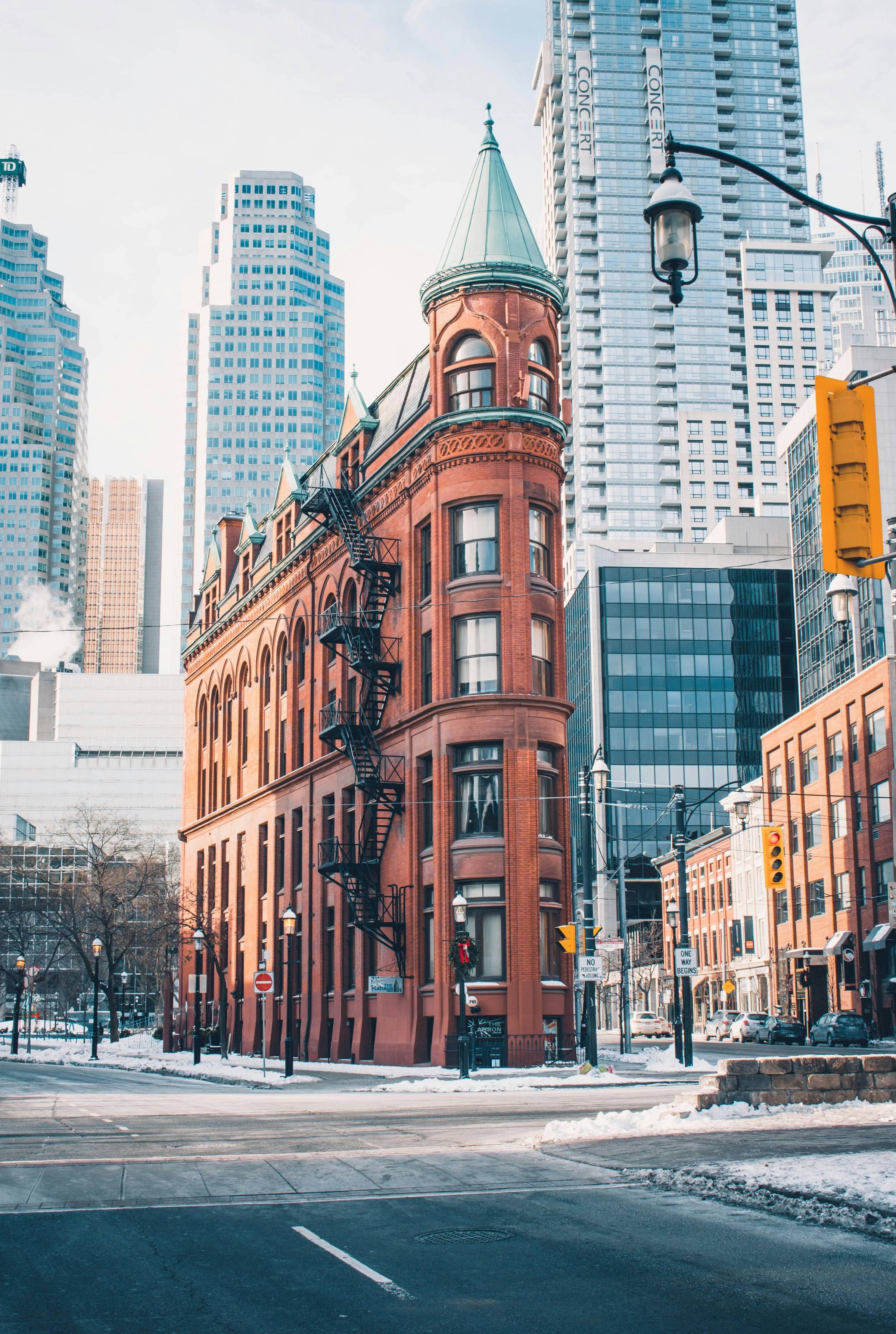 The red-brick Gooderham Building's narrow wedge on a snowy morning, with downtown glass towers behind it.