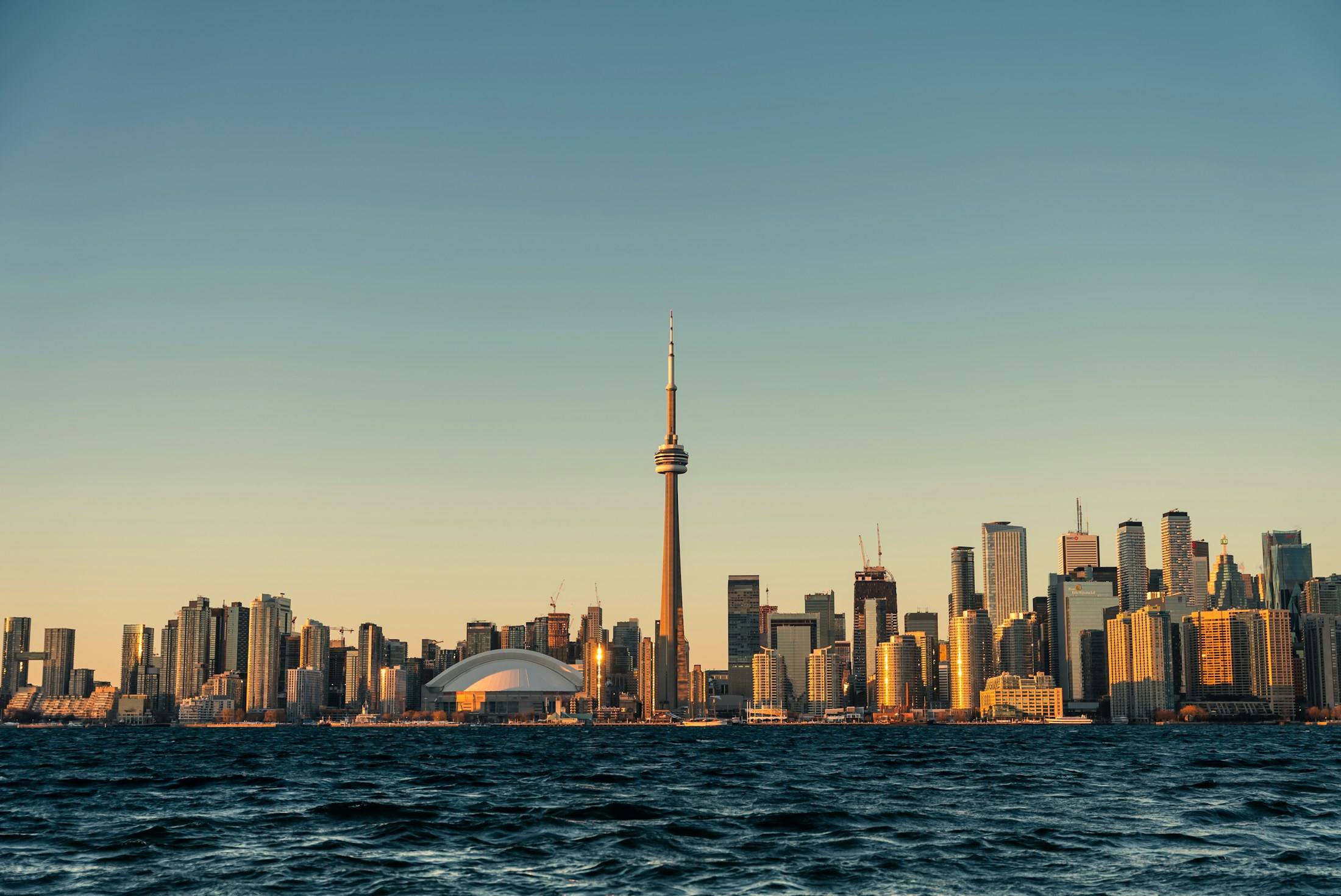 The Toronto skyline and CN Tower at golden hour, seen across Lake Ontario.